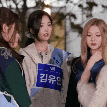 a girl wearing a blue vest with s5 on it talks to two other girls