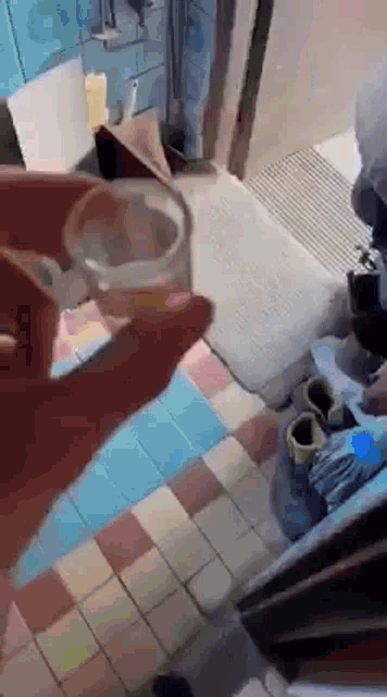 a person is holding a glass of water in their hand in a kitchen .