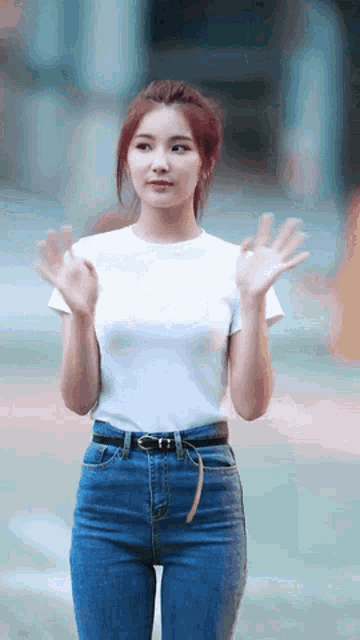 a woman in a white t-shirt and blue jeans is waving