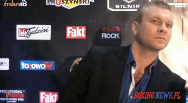 a man in a suit stands in front of a wall with boxing news.pl written on it