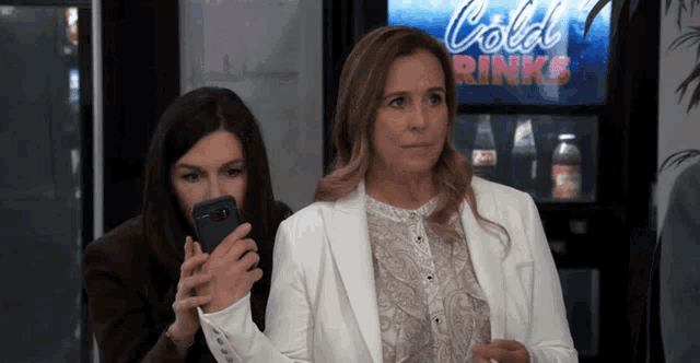 two women are standing in front of a cold drink machine