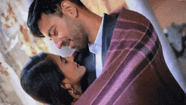 a man and woman are kissing under a purple blanket