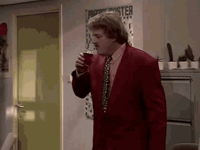 a man in a red suit and tie is drinking from a cup .