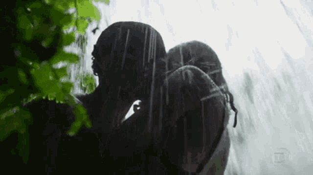 a man and woman are kissing in the rain in front of a waterfall .