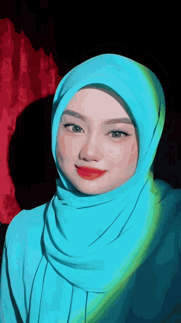 a woman wearing a blue hijab and red lipstick looks at the camera