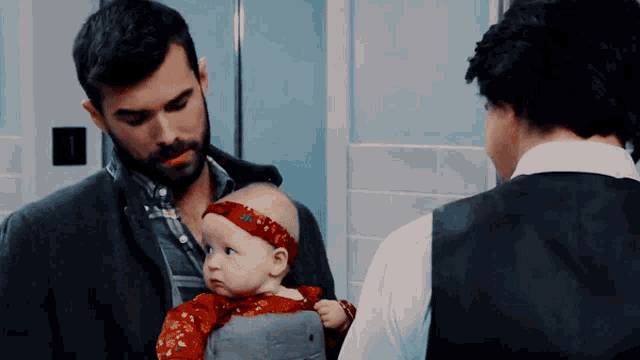 a man is holding a baby in a carrier and talking to another man