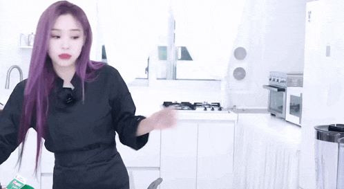 a woman with purple hair is dancing in a kitchen while holding a green box .