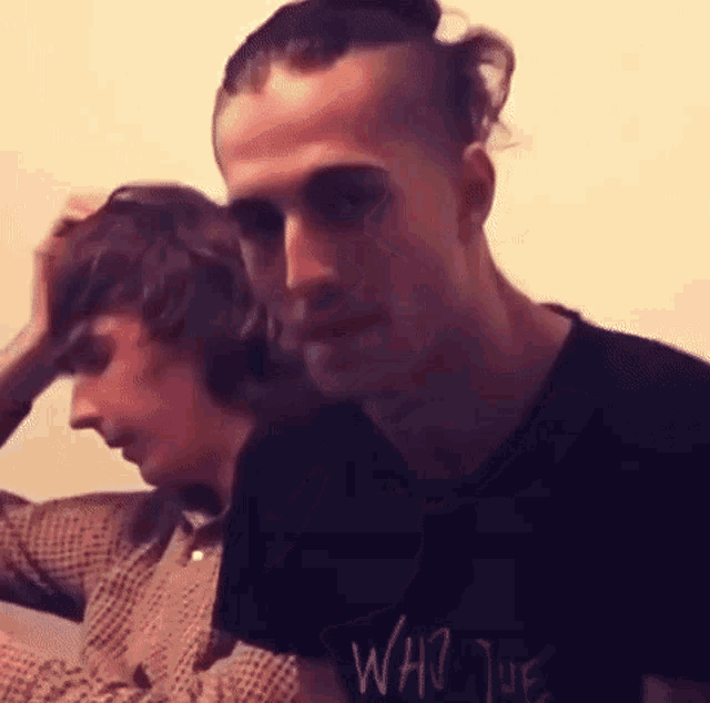 two men are sitting next to each other and one of them is wearing a black shirt that says who the