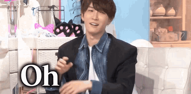 a man in a denim jacket is sitting on a white couch with the word oh written on the bottom