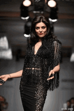 a woman is walking down the runway at a fashion show wearing a black dress .