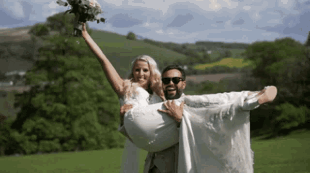 a man is carrying a bride in his arms and she is holding a bouquet of flowers .