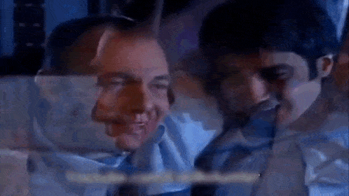 two men are sitting next to each other in a dark room and smiling .