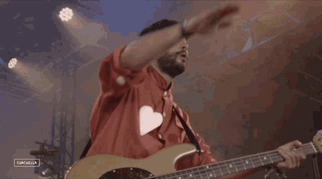 a man wearing a red shirt with a heart on it is playing a guitar with a coachella logo in the corner