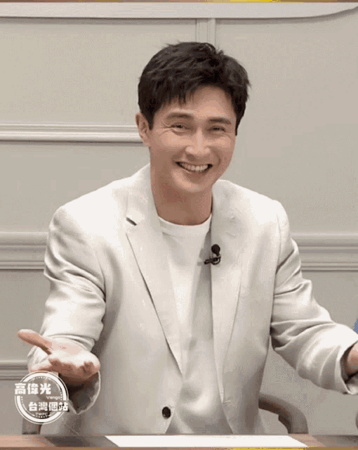 a man wearing a white jacket with a microphone on his neck is smiling