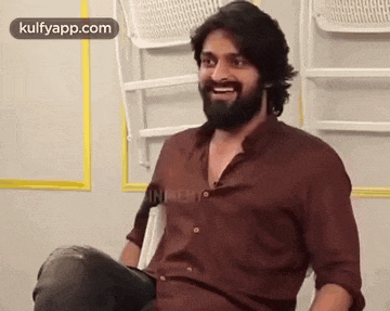 a man with a beard is sitting in a chair laughing .