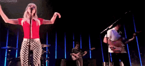 a woman is singing into a microphone while a man plays a guitar on a stage .