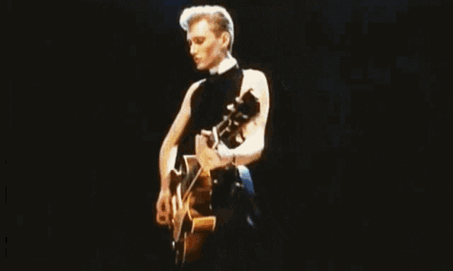 a man in a black tank top is playing a guitar on stage .