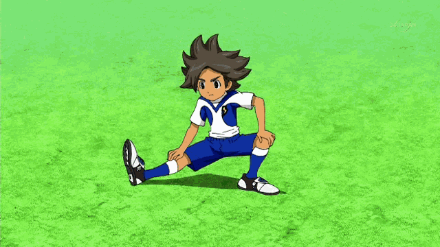a boy in a blue and white uniform stretches his legs on a soccer field