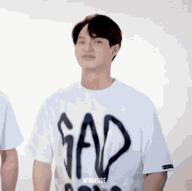 a young man wearing a white gap t-shirt is standing in front of a white background .