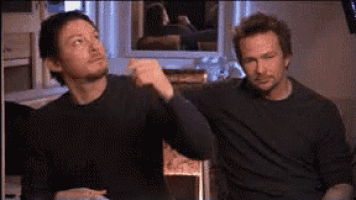 two men are sitting next to each other on a couch and one of them is pointing at something