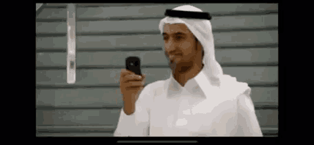 a man in a white shirt is holding a cell phone and smiling