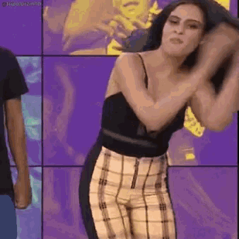 a woman in a black top and plaid pants is dancing in front of a purple background .