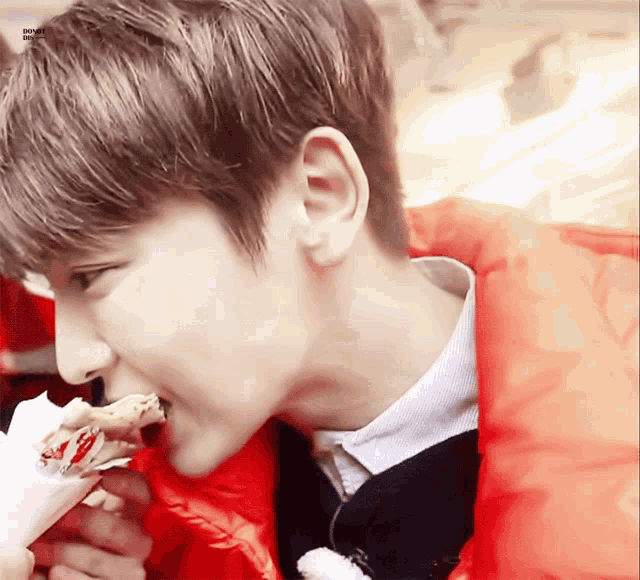 a young man in a red jacket is eating a chicken nugget