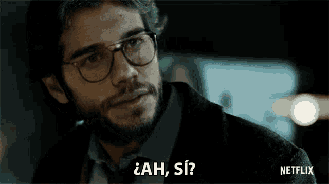 a man with glasses and a beard is asking a question in a foreign language .