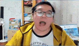 a man wearing glasses and a yellow jacket is making a funny face while looking at the camera .