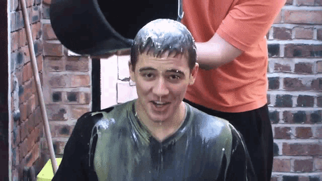 a man in an orange shirt is pouring a bucket of liquid on a man 's head