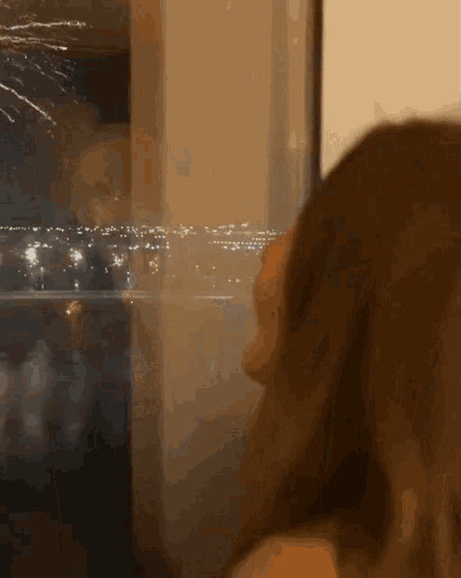 a woman looks out of a window at fireworks