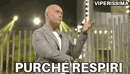 a bald man in a suit is standing in front of a stage with his hands in the air and says purche respiri .
