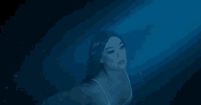 a woman in a white tank top is swimming in the ocean .
