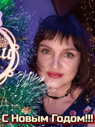 a woman stands in front of a christmas tree with a greeting in russian on the bottom