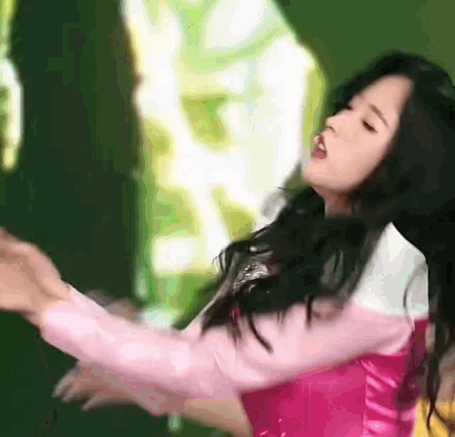 a woman in a pink shirt is dancing in front of a green background .