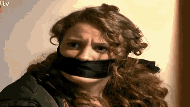 a woman with a black ribbon around her mouth looks at the camera