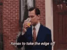 a man in a suit and tie is drinking a glass of orange juice and says xanax to take the edge off .