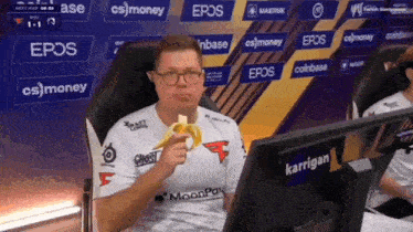a man is eating a banana while sitting in front of a screen that says karrigan