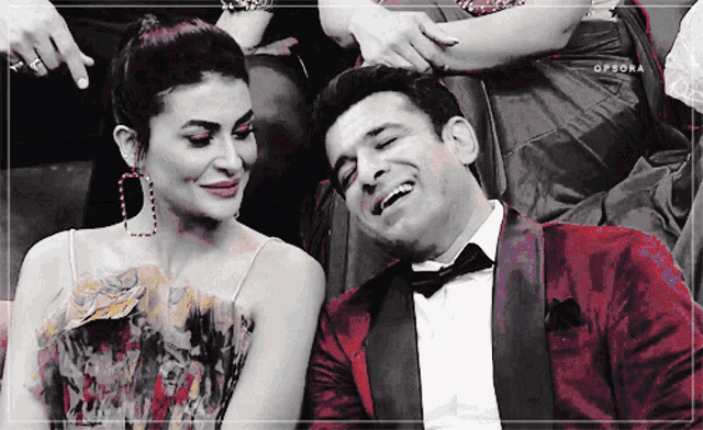 a man in a tuxedo and a woman in a dress are sitting next to each other and laughing