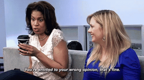 two women are sitting on a couch talking to each other and one woman is holding a cup of coffee .