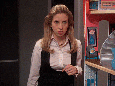 a woman in a white shirt and black vest stands in front of a dollhouse