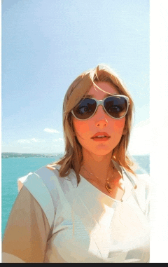 a woman wearing sunglasses and a white shirt stands in front of a body of water