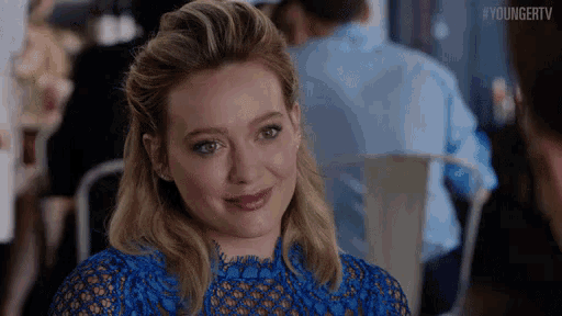 a woman in a blue lace dress is smiling while sitting at a table in a restaurant .