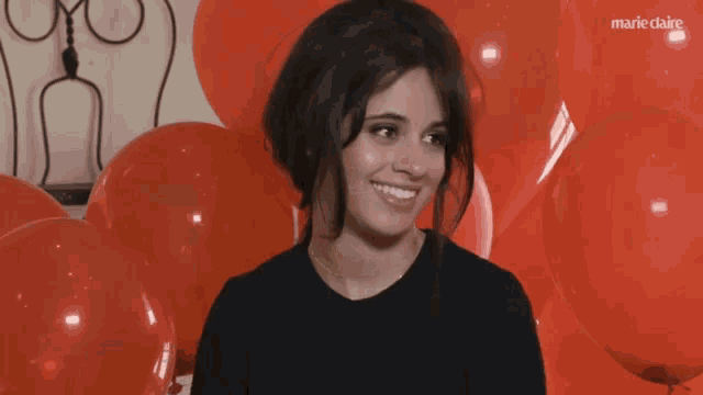 a woman stands in front of a bunch of red balloons with marieclaire written on the bottom