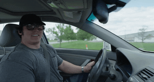 a man wearing sunglasses and a black hat is driving a car