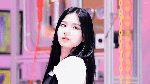 a young woman with long black hair is standing in front of a pink wall .