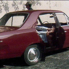 a man is sitting in a red car with his legs out the door