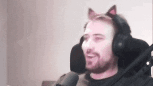 a man wearing cat ears is sitting in front of a microphone and smiling .