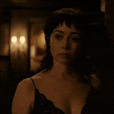 a woman in a black lace tank top stands in a dark room