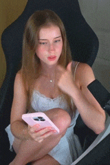 a woman in a white dress is sitting in a chair holding a pink cell phone and giving a thumbs up